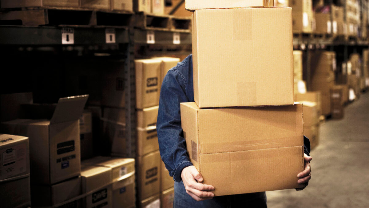 A warehouse working carrying a stack of cardboard boxes inside a warehouse.