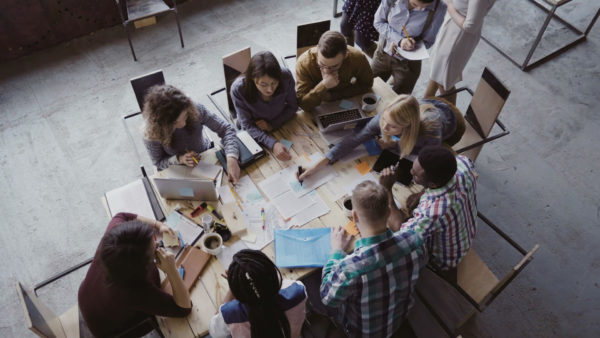 Top-view-of-mixed-race-business-team-sitting-at-the-table-at-loft-office-and-working.-Woman-manager-brings-the-document-681735120_3840x2160